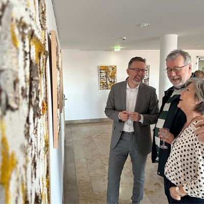 Zwei M&auml;nner und eine Frau stehen vor einer Wand, an der gro&szlig;formatige Bilder h&auml;ngen.