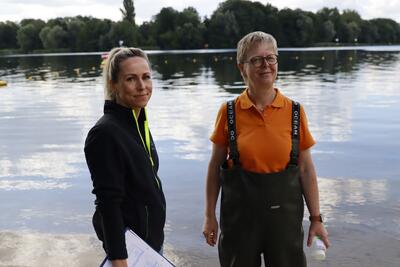 Zwei Frauen stehen an einem See, um die Wasserqualität mittels Proben zu testen.                                                                              