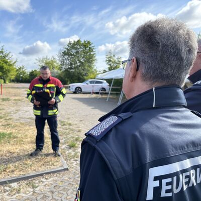 Zwei Männer mit dunklen Jacken und dem Aufdruck Feuerwehr rechts vorne im Bild.