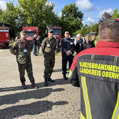 Im Bildvordergrund steht ein männlicher Kreisbrandmeister vom Landkreis Oberhavel. Im Hintergrund mehrere Männer.
