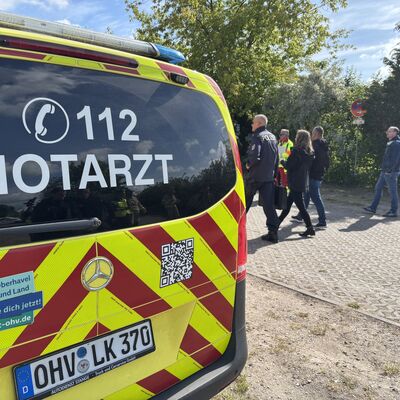 Zu sehen ist ein gelb-rotes Notarztfahrzeug des Landkreises Oberhavel mit der Telefonnummer des Notarztes 112 auf der Heckscheibe.