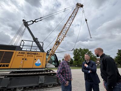 Drei Männer stehen vor einer Planierraupe mit dem Aufdruck HS 8040. 