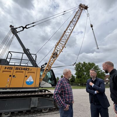 Drei Männer stehen vor einer Planierraupe mit dem Aufdruck HS 8040.