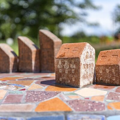 Fünf Ziegel in Form von Häusern stehen auf einem bunten Mosaikfeld.