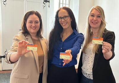Drei Frauen zeigen lächelnd einen Organspendeausweis in die Kamera.
