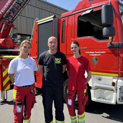 Drei Personen stehen vor einem Feuerwehrfahrzeug der Freiwilligen Feuerwehr Leegebruch. Zwei Frauen und ein Mann.