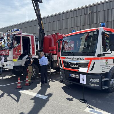 Auf dem Bild sind Einsatzfahrzeuge der Feuerwehr und des Katastrophenschutzes  zu sehen. Zwei Personen, stehen im Gespräch vor den Fahrzeugen.