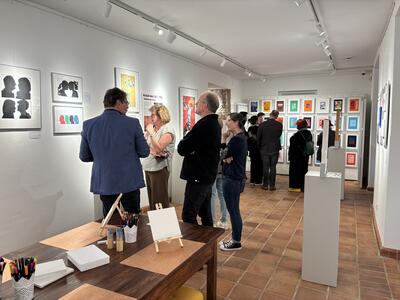 Männer und Frauen stehen in einer Galerie und betrachten Bilder an einer Wand. 