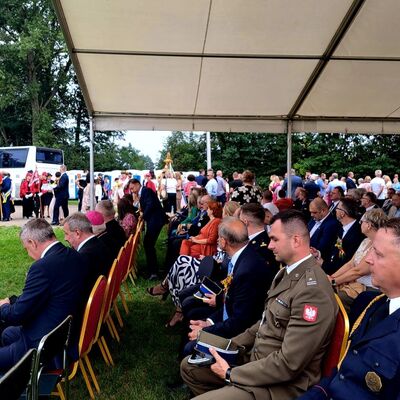 Männer in Uniformen und Anzügen sitzen in Stuhlreihen auf einer Festwiese unter einem Festzelt.