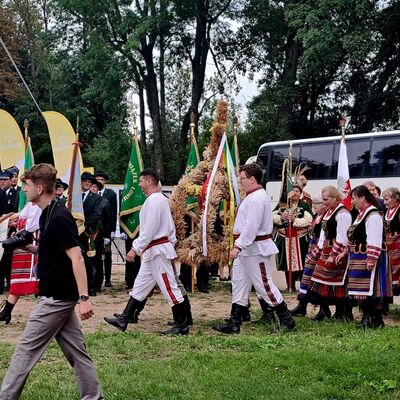 Männer und Frauen in traditioneller, polnischer Tracht laufen über eine Wiese. Im Hintergrund ein weißer Reisebus.