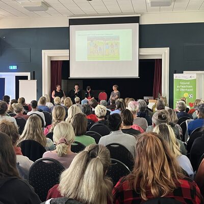 Kathleen Kunath sitzt auf der B&uuml;hne und spricht gemeinsam mit jungen Menschen, die vom Fetalen Alkoholsyndrom betroffen sind, vor den Teilnehmerinnen und Teilnehmer der FASD-Expertenveranstaltung.