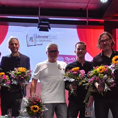 Die drei Autoren Richard Brandes, Sven Stricker und Andreas Winkelmann, der Moderator Vincent Kliesch und die drei Musiker der Pankeperlen auf der Bühne mit den zuvor überreichten Blumensträußen.