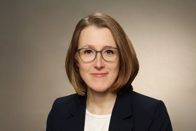 Eine Frau mit Brille mittleren Alters mit dunkelblonden, kinnlangen Haaren, schwarzem Sakko und weier Bluse.