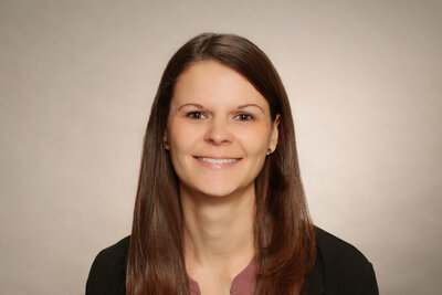 Eine Frau mit offenen, dunkelbraunen, langen Haaren, schwarzem Sakko und weinroter Bluse.