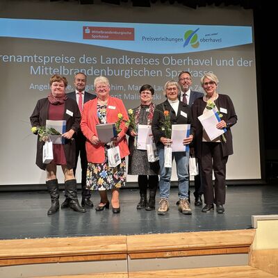 Mehrere Männer und Frauen mit Urkunden in den Händen auf einer kleinen Theaterbühne.