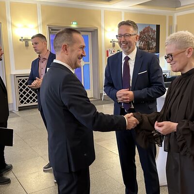 Männer und eine Frau auf einem Stehempfang bei einer Begrüßung.