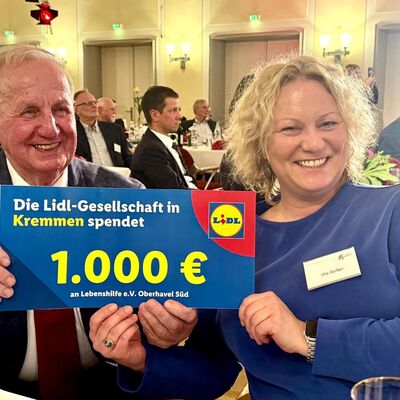 Ein Mann und eine Frau halten einen symbolischen Spendenscheck der Lidl-Gesellschaft über 1.000 Euro in die Kamera.