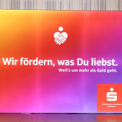 Ein Banner mit buntem Farbverlauf und der Aufschrift: Wir fördern, was du liebst. Absender ist die Mittelbrandenburgische Sparkasse (MBS).
