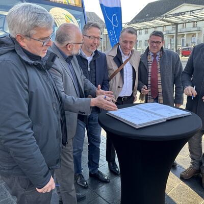 Sechs Männer mittleren Alters stehen um einen schwarzen Stehtisch  Im Hintergrund ein Verkehrsbus und eine Beachflag mit dem Logo vom Landkreis Oberhavel.