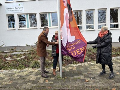 Zwei Frauen und ein Mann mittleren Alters hissen eine Aktionsflagge. 
