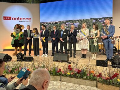 Eine Delegation aus M&auml;nnern und Frauen steht auf einer B&uuml;hne auf der Gr&uuml;nen Woche 2026 des Radiosenders Antenne Brandenburg. 