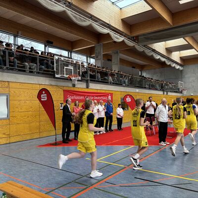 M&auml;dchen im Teeniealter laufen in gelben, kurzen Trikots &uuml;ber einen Turnhallenboden ein.