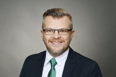 Ein Mann mittleren Alters mit kurzen dunkelblonden Haaren, Brille und dunklem Jacket, wei�em Hemd und einer gr�nen Satinkrawatte.