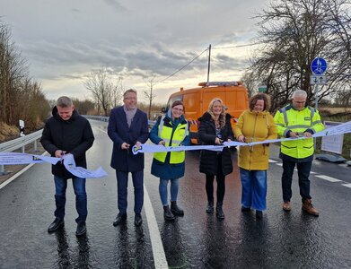 Drei M&auml;nner und drei Frauen stehen auf einer Stra&szlig;e und schneiden ein Sperrband durch. 