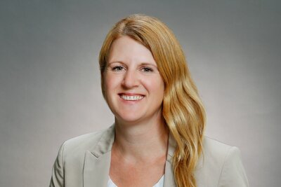 Eine Frau mittleren Alters mit langen, blonden Haaren und einen beigefarbenen Sakko lacht in die Kamera.
