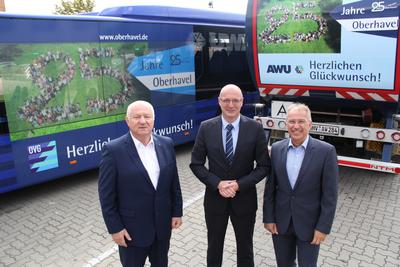 Klaus-Peter Fischer, Ludger Weskamp und Manfred Speder (von links nach rechts) vor Bussen und AWU-Fahrzeugen, die f&uuml;r das Landkreis-Jubil&auml;um werben.
